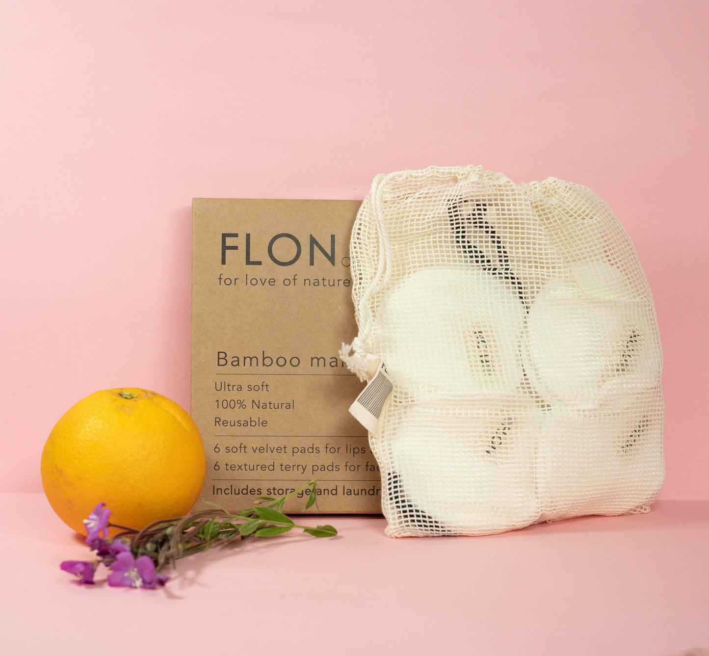 Reusable bamboo makeup pads arranged with an orange and flowers on a pink background.