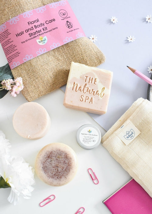 Floral hair and body care starter kit with solid shampoo, conditioner and soap, in a pink-labeled jute bag, on a light background with flowers.