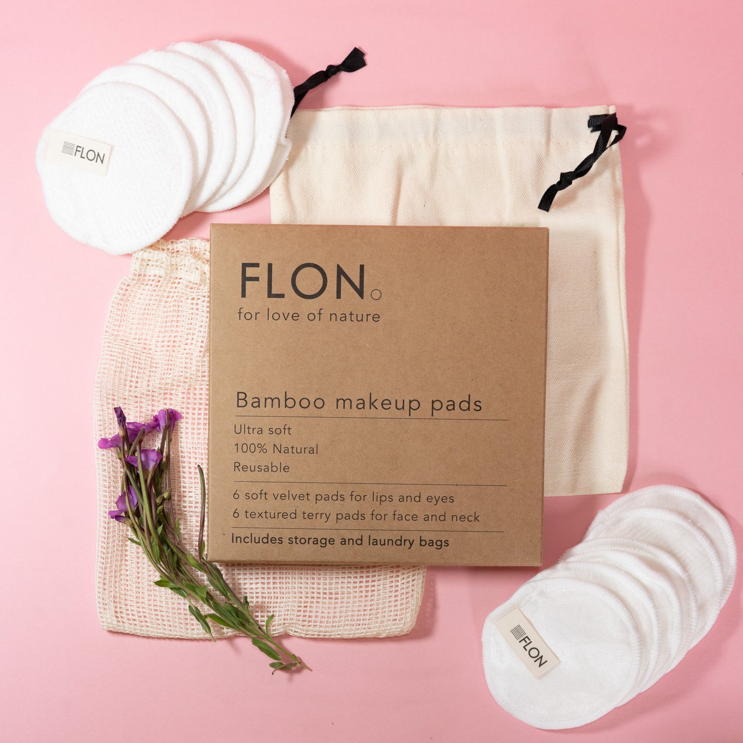 Set of bamboo makeup remover pads and cardboard packaging on a pink background with flowers.