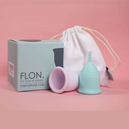 Two reusable menstrual cups with box and pouch on soft pink background.