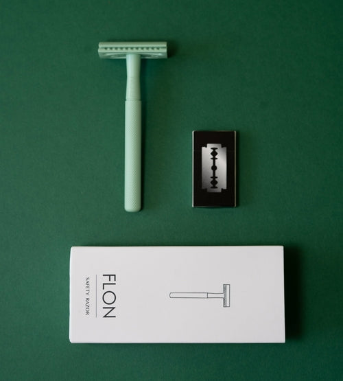 Reusable safety razor in green brass finish with eco-friendly box on green background.