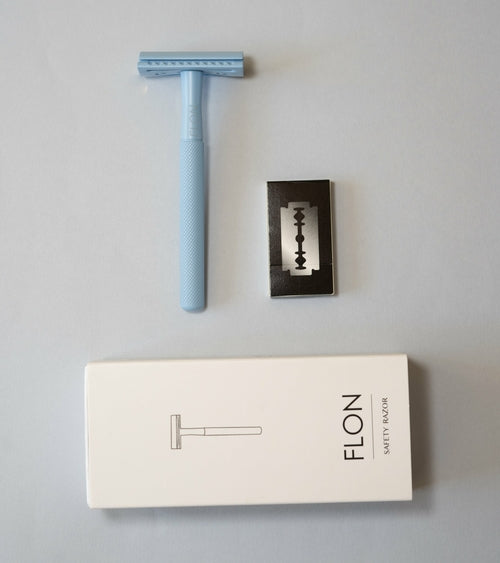 Light blue reusable safety razor with stainless blade and FLON packaging on grey background.