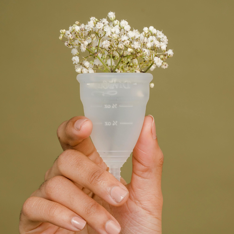 Hand holding a menstrual cup filled with white flowers, symbolising sustainable hygiene and self-care.