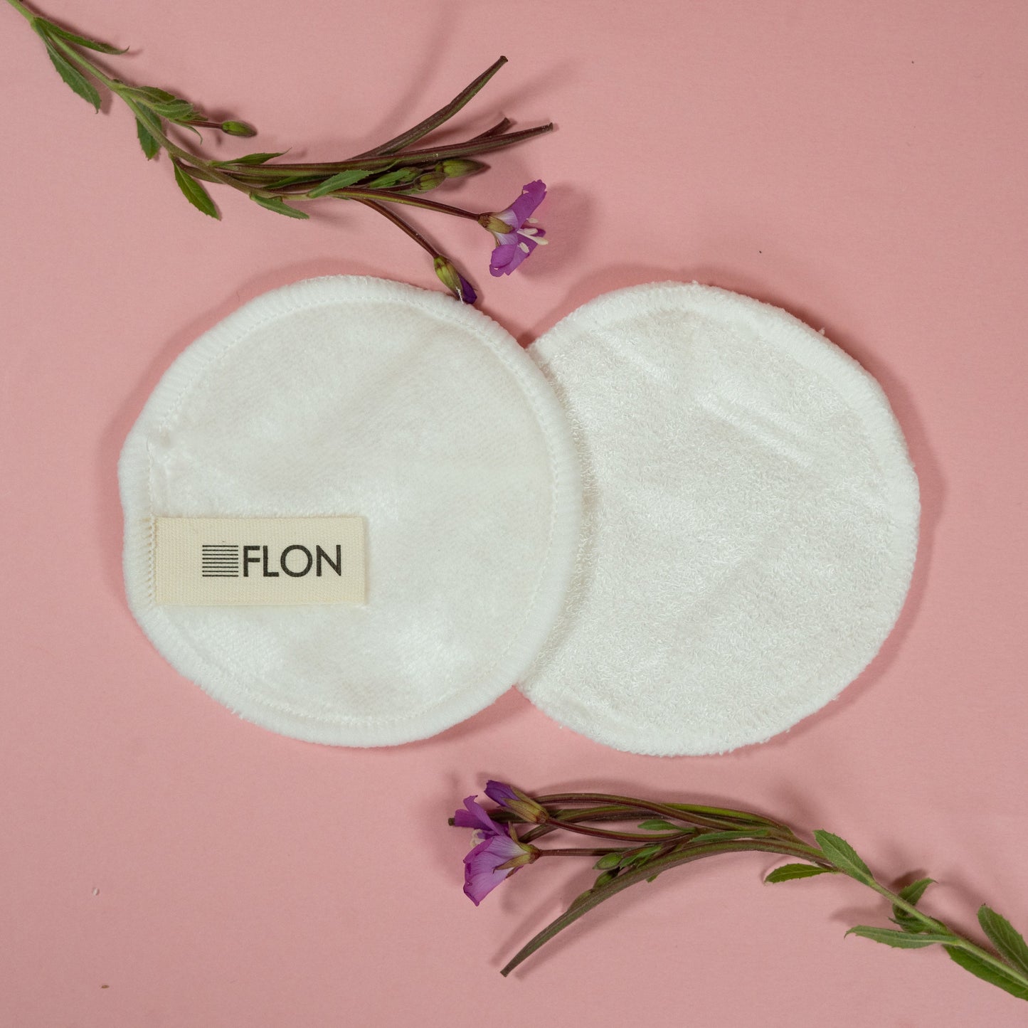 Bamboo makeup remover pads and box styled with flowers on a pink surface.
