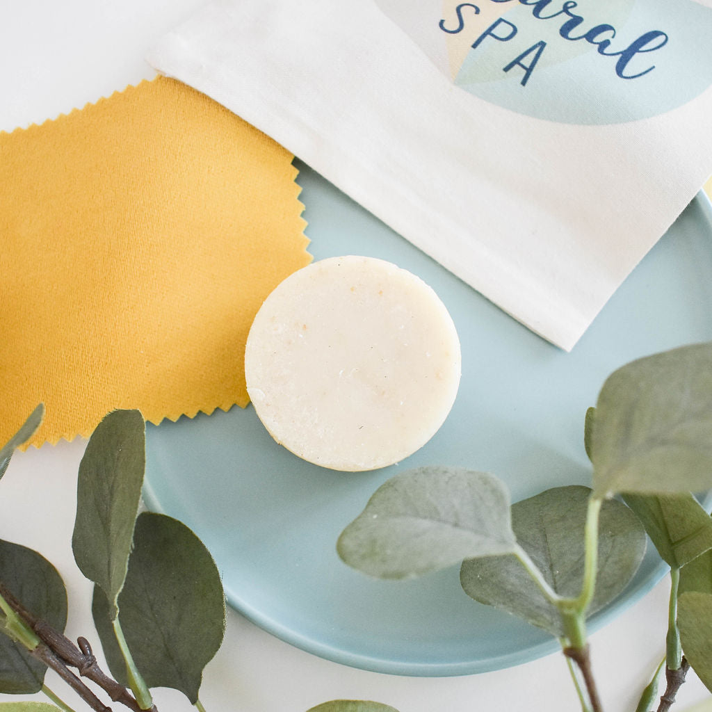 Handmade eucalyptus and lemon shampoo bar on white background with yellow towel and greenery.