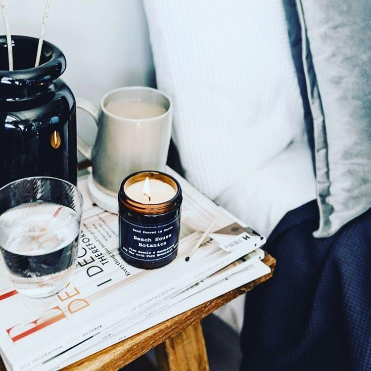 Orange & cinnamon soy wax candle in a cosy setting with mug and glass on a wooden table.