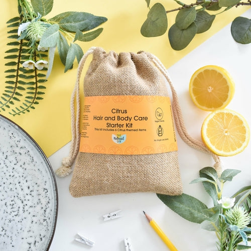Citrus hair and body care starter kit in a reusable jute bag with orange label, styled with lemons and greenery on a yellow background.