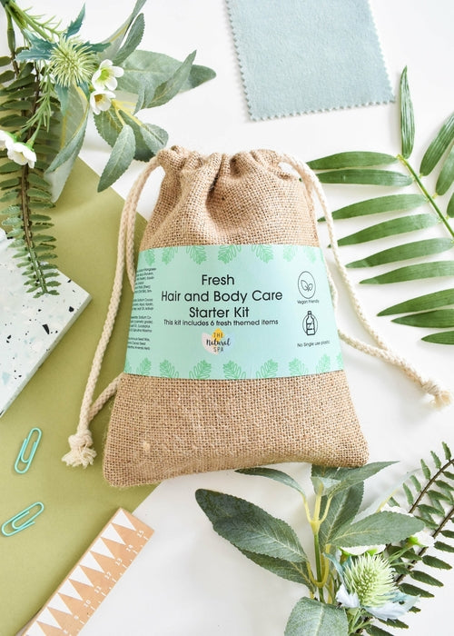 Fresh hair and body care starter kit in a reusable jute bag with green label, styled with tropical leaves.