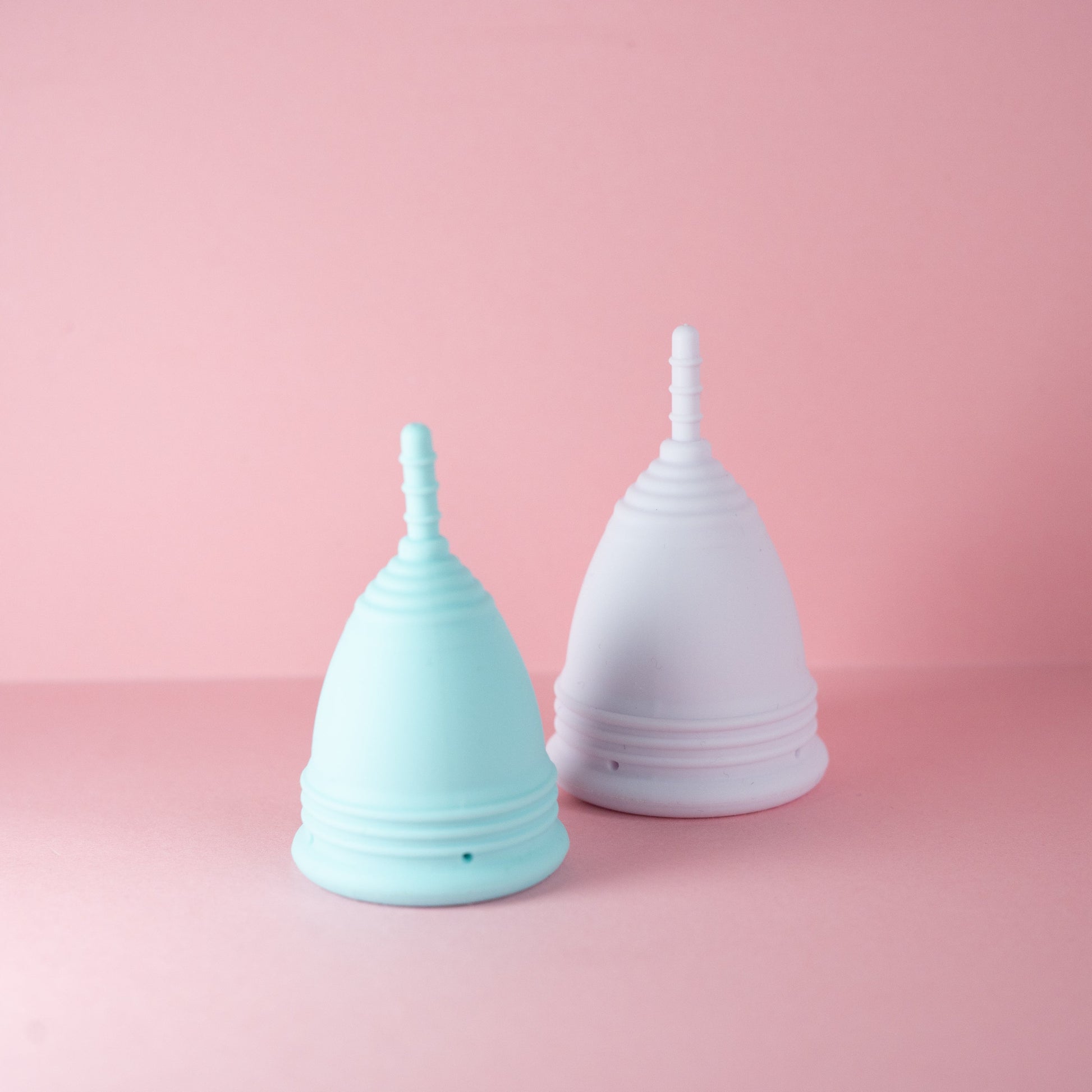 Two menstrual cups in different sizes on pink background.