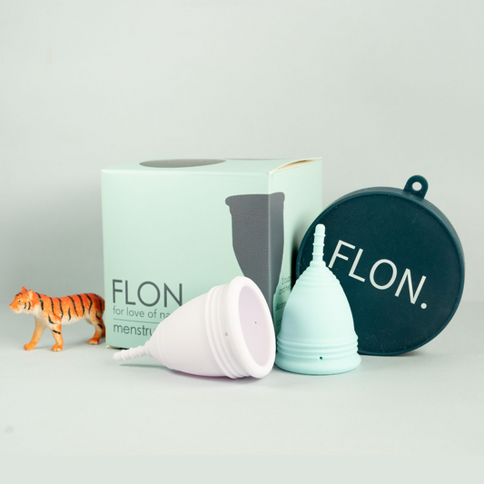 Reusable menstrual cup set with two cups, storage pouch and box on light background.