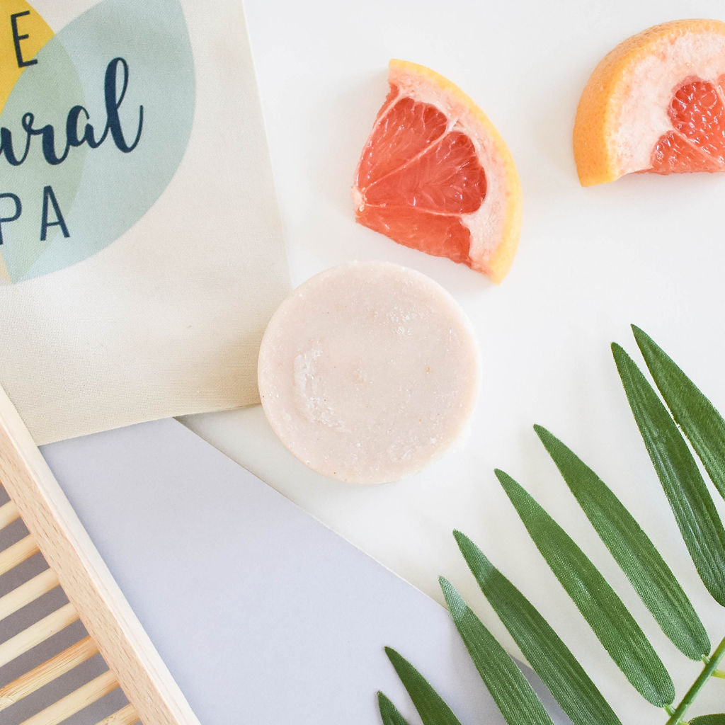Vegan solid shampoo bar with rose, lavender and grapefruit oils, styled with tropical leaves and grapefruit slices. Sustainable and plastic-free.